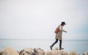 A person walking across rocks in front of the sea